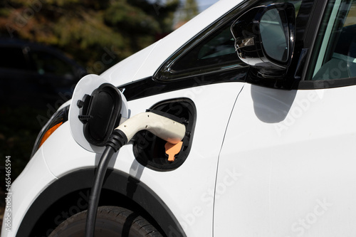 Closeup of a white electric car charging at a public charging station on a sunny day.