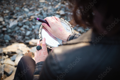 Rear view of a female holding a mirror and a lipstick outdoors photo