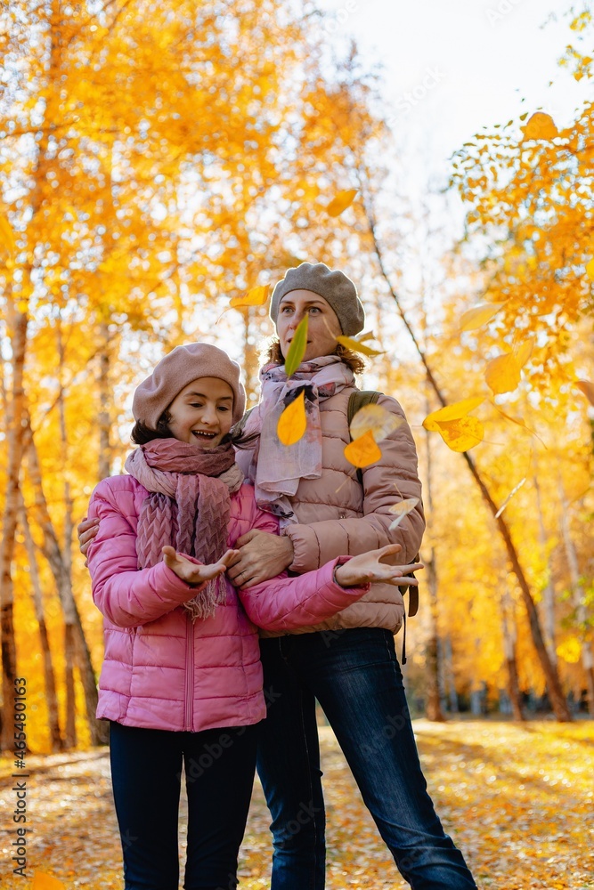 A happy family. Cute and joyful smiling caucasian mom and daughter spend time in the autumn park. Walking in the park with children. Sunny fall day. Positive emotions. Vertical shot A happy family. Cute and joyful smiling caucasian mom and daughter spend time in the autumn park. Walking in the park with children. Sunny fall day. Positive emotions. Vertical shot