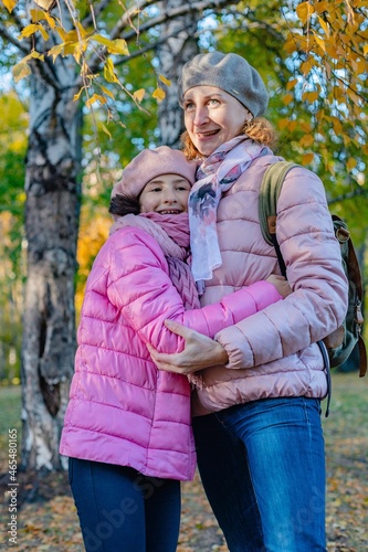 Cute and joyful smiling caucasian mom and daughter spend time in the autumn park. A happy family. Walking in the park with children. Sunny fall day. Positive emotions. Vertical shot