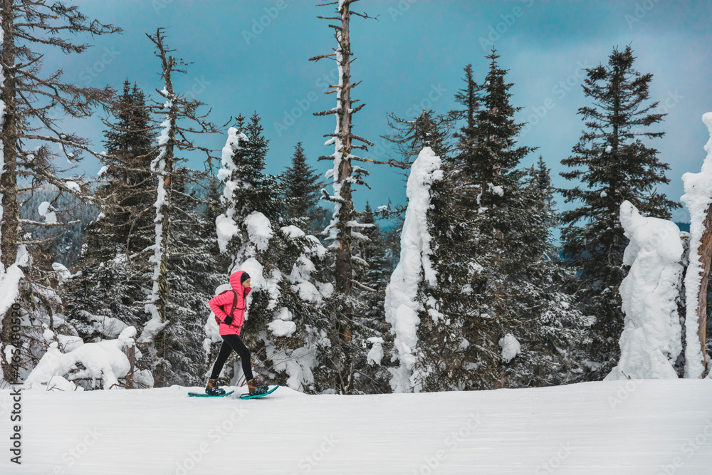 Snowshoe winter sport woman hiking on snow trail in winter cold outdoors day snowshoeing alone walking uphill mountain.