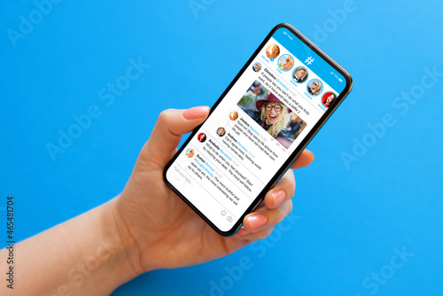 Person holding mobile phone in hand on blue background with sample social media microblogging app on the screen photo