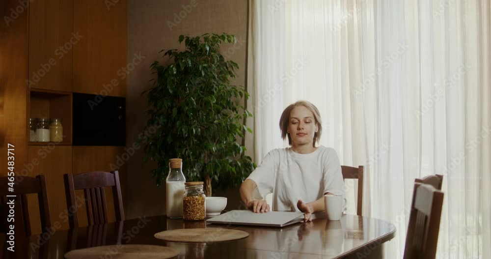 Young woman sits down at the breakfast table, opens a laptop and drinks coffee Young woman sits down at the breakfast table, opens a laptop and drinks coffee