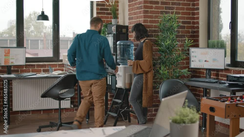Colleagues on break having discussion and using water cooler in business office. Man and woman talking while drinking cup of water as refreshment, using liquid dispenser for hydration Colleagues on break having discussion and using water cooler in business office. Man and woman talking while drinking cup of water as refreshment, using liquid dispenser for hydration