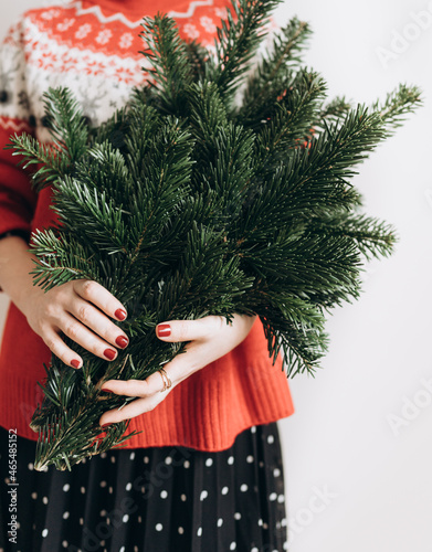 a modern woman in a red sweater with fir branches in her hands at Christmas on a light background. The minimum concept of the new year. no face