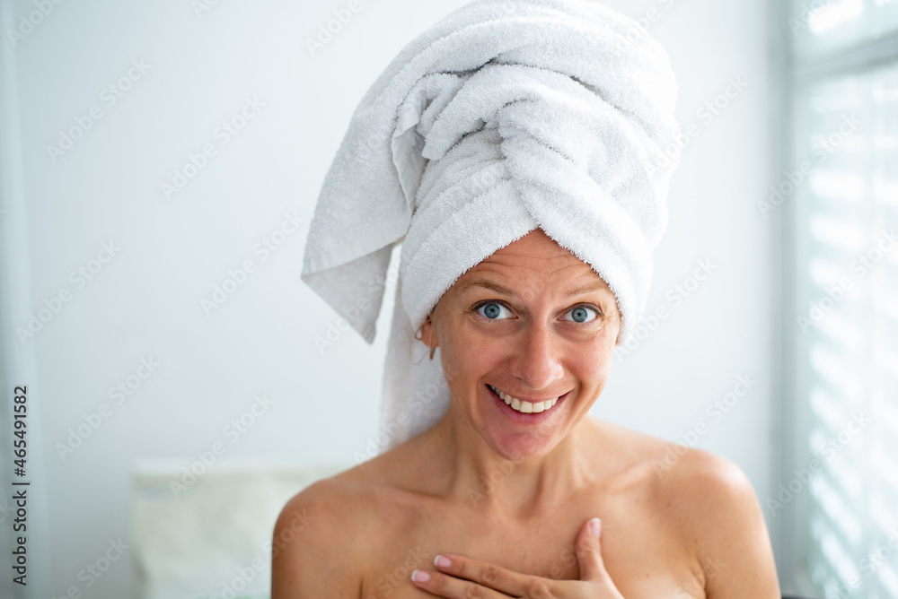 Woman with bare shoulders and white towel on head, cute face and nice smile. Girl hold hand on chest. Beauty salon. Skin, hair and body care. Time after shower. Woman with bare shoulders and white towel on head, cute face and nice smile. Girl hold hand on chest. Beauty salon. Skin, hair and body care. Time after shower.