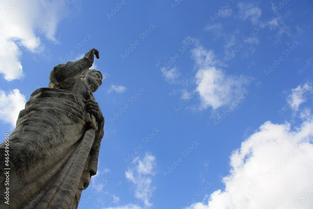 Old giant statue in front of the Basilica of Saints Peter and Paul in EUR district, Rome. the apostle Peter with the keys in his hand. Low angle view on cloudy sky.