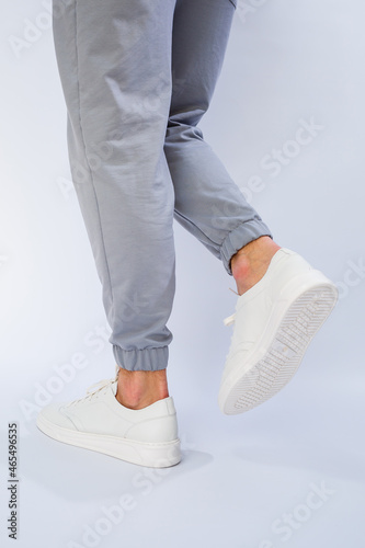 Men's feet in white everyday sneakers made of natural leather on lacing.