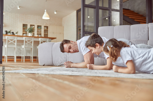 Low angle of sporty man training core toether with sun and daughter in living room photo