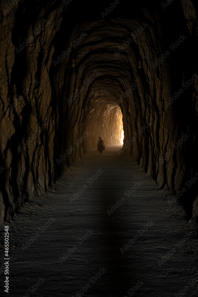 human shilouette walking inside a deep and dark tunnel carved in the stone