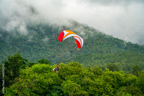 The sportsman on a paramotor gliding and flying in the air with majestic clouds and green forest are background. Paramotor it is extreme sport. photo