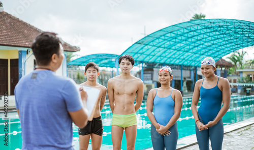four teenage swimmers in swimsuits standing with trainer