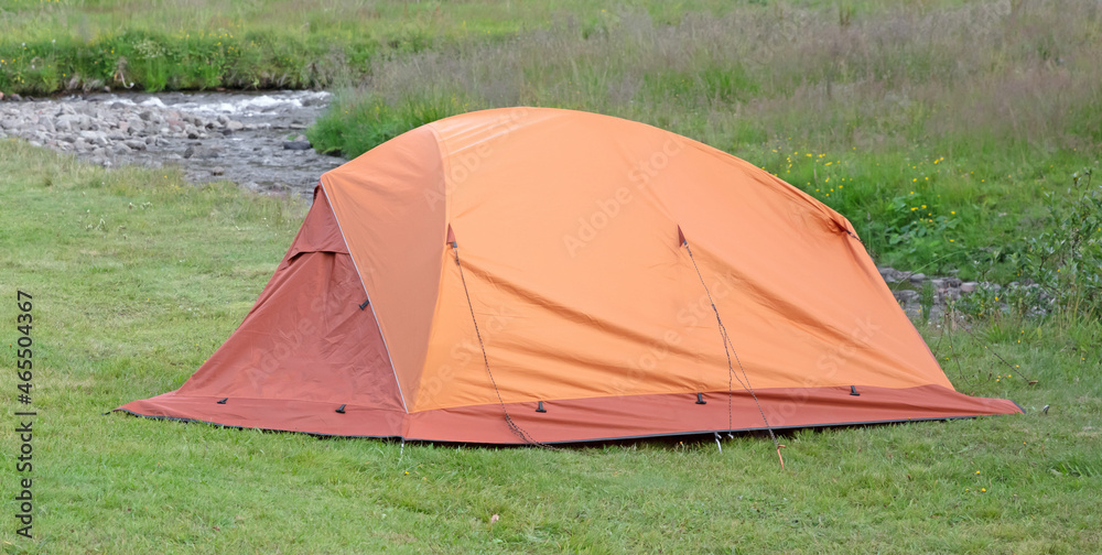 Orange dome tent on green grass in camping site