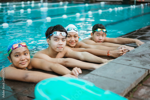 four smiling teenagers in swimsuits while resting by standing by the pool