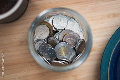Canadian toonie loonie and quarter money in jar on a desk