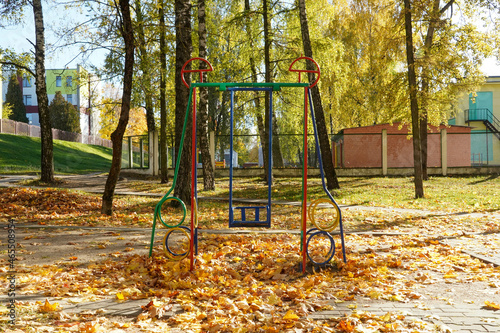 Photo of a swing for children on the street in the courtyard in the city in autumn with yellow fallen maple leaves
