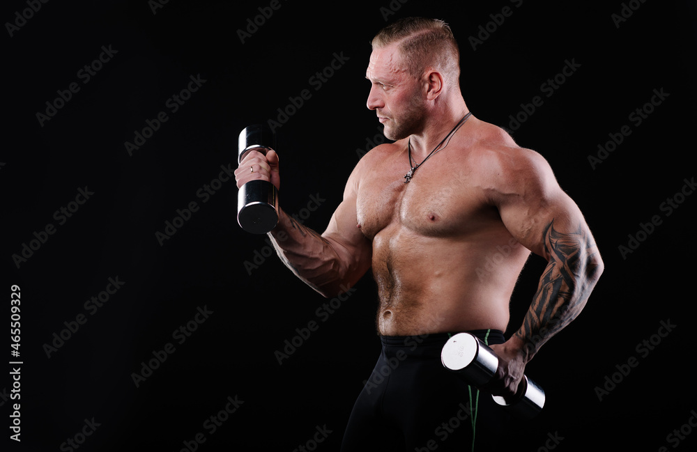 Strong tanned muscular man goes in for sports. An athlete with a naked torso and strong muscles. Muscular arms. Fitness trainer bodybuilder. Black background. Tattooed arms sleeves. gym motivation