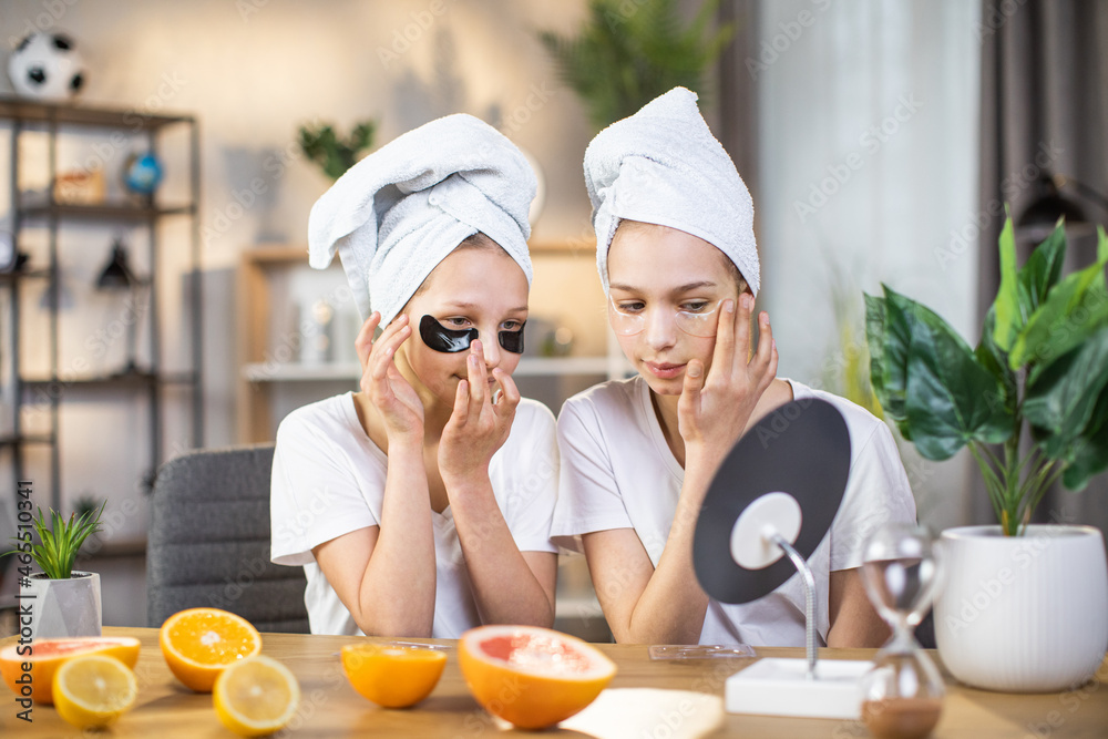 Two caucasian teen sisters with towel on had taking care of soft skin under eyes using collagen patches. Concept of youth, beauty routine and healthy lifestyles. Two caucasian teen sisters with towel on had taking care of soft skin under eyes using collagen patches. Concept of youth, beauty routine and healthy lifestyles.