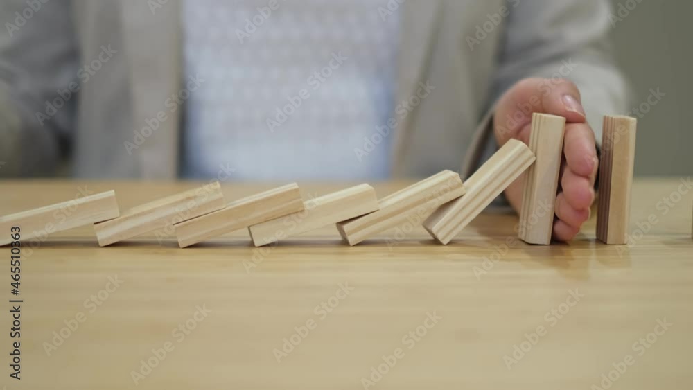 businessperson hand stopping colorful blocks from falling on table in office. domino effect in business.