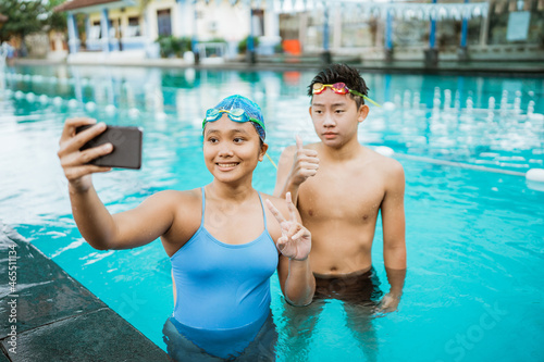women and young men smiling while taking selfie with a smartphone in the swimming pool © Odua Images