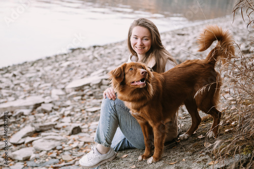 young woman and dog retriever walks on river shore at autumn season