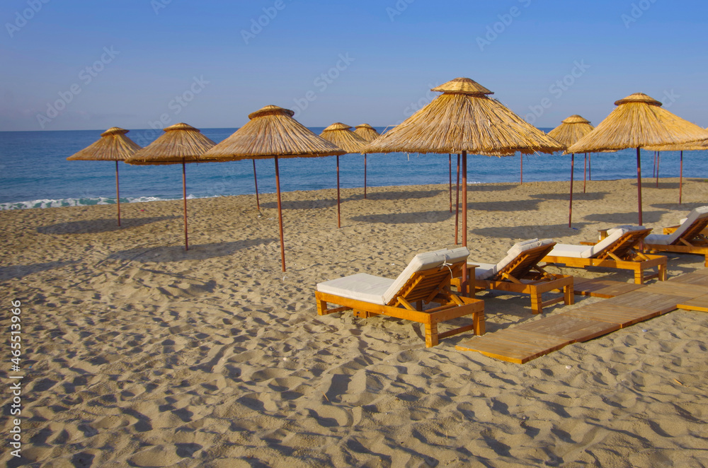 Thatched umbrellas and sun loungers on an empty beach by the sea.