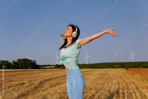 beautiful young middle age woman breathing fresh air with open arms feeling freedom with helmets in the cereal field with windmills in the background.