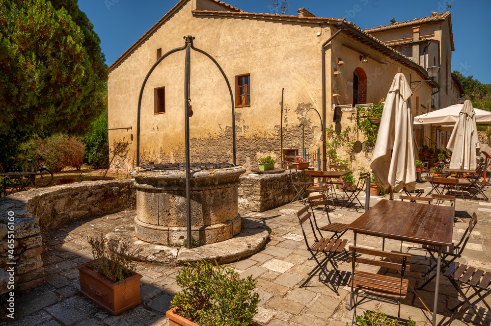 Bagno Vignoni, Tuscany, Italy. August 2020. In the center of the village a restaurant with outdoor tables and umbrellas, an ancient well gives the context a lot of charm.