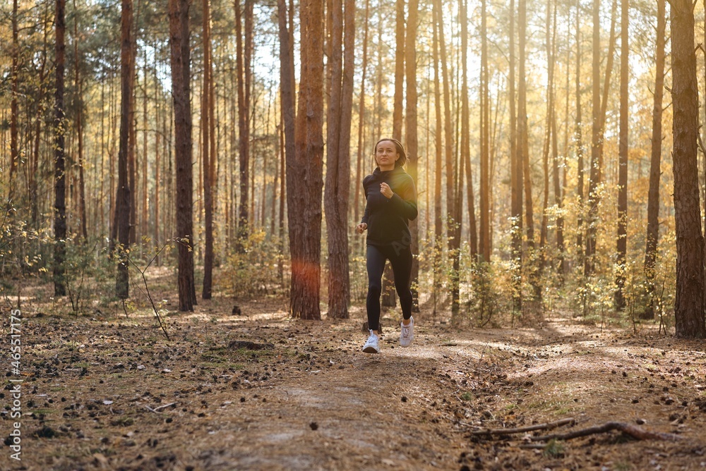 Young athletic woman jogging in forest in sunny morning. Healthy lifestyle concept. Young athletic woman jogging in forest in sunny morning. Healthy lifestyle concept.