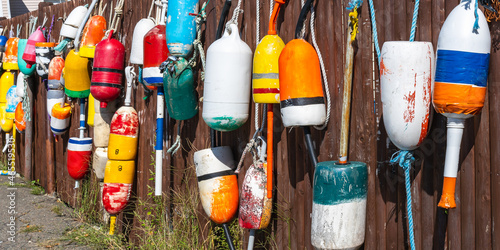 A brown wooden fence decorated with old lobster floats in the Atlantic Ocean as a symbol of the fishing village