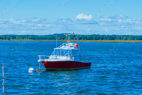 A white boat with red sides in windy weather is moored at the mouth of a river near the Atlantic Ocean