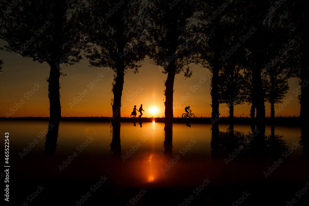 Man and woman running after bicycle at sunset between trees. Couple in evening following cyclist. Man and woman running after bicycle at sunset between trees. Couple in evening following cyclist.