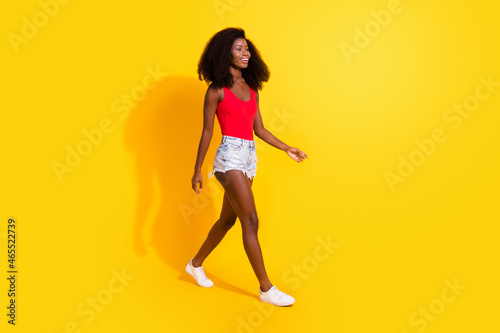 Full length body size profile side view of attractive cheerful thin girl walking wearing season clothes isolated over bright yellow color background © deagreez