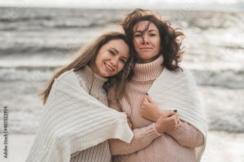 close friends support each other. the sisters walk together by the sea in the fall. the girls wrapped themself in a warm and cozy blanket. sincere love between people.  photo
