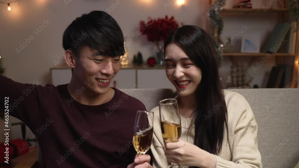 young asian korean couple indoors at home at Christmas eve. woman and man celebrating xmas having video call with family. happy female and male cheers with glasses of wine and enjoy drinking young asian korean couple indoors at home at Christmas eve. woman and man celebrating xmas having video call with family. happy female and male cheers with glasses of wine and enjoy drinking