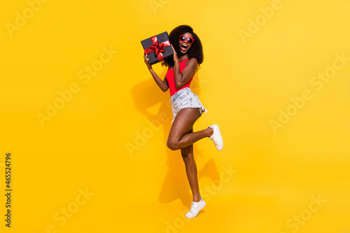 Full length body size view of attractive cheerful girl holding in hands black giftbox isolated over bright yellow color background