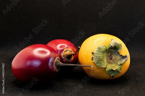 Stillleben mit Südfrüchten - Eine Kakifrucht und zwei Grenadillas,  freigestellt vor schwarzem Hintergrund photo