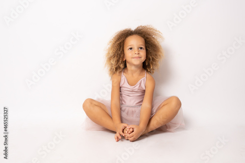 Beautiful little ballerina sitting on floor isolated over white background