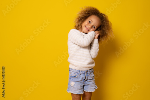 Beautiful little child girl sleep gesture posing with hands together smiling with looking at camera isolated over yellow background.