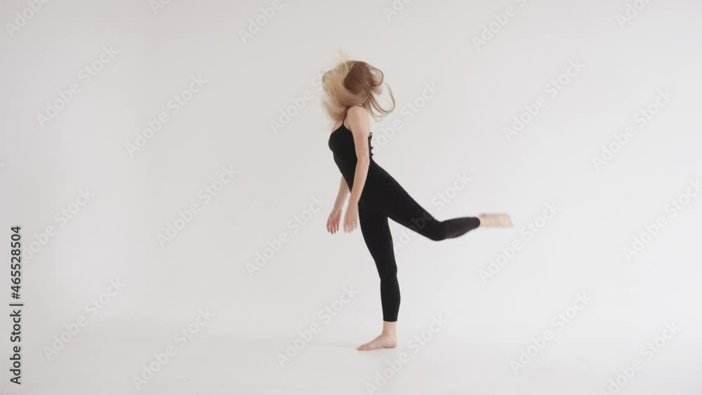An energetic young girl in tight black clothes makes a swing leg and takes a vertical split. Harmony and balance concept An energetic young girl in tight black clothes makes a swing leg and takes a vertical split. Harmony and balance concept