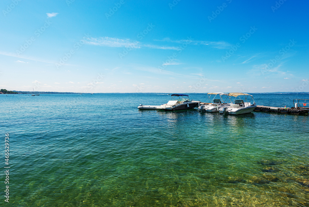 Group of small speedboats moored on the coast of Lake Garda (Lago di Garda) in front of the Bardolino village, tourist resort in Verona province, Veneto, Italy, Europe. Lombardy coast on the horizon.