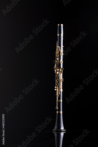 A full size clarinet with gold plated keys on a reflective surface and a black background. A woodwind instrument common to classical music.