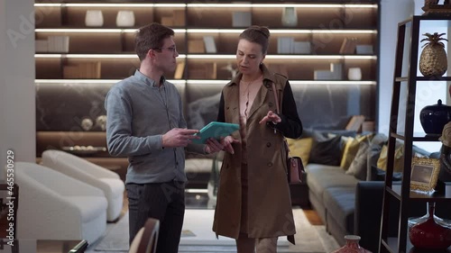 Wide shot portrait elegant woman and confident man with tablet walking in luxurious showroom talking choosing furniture discussing purchase. Positive buyer and seller in furnishings store indoors