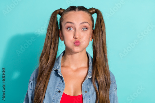 Photo of funny childish young woman dressed denim jacket ponytails bloated cheeks isolated teal color background photo