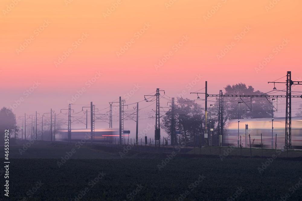 Traffic on electrified railroad track at foggy autumn morning. Trains in blurred motion..