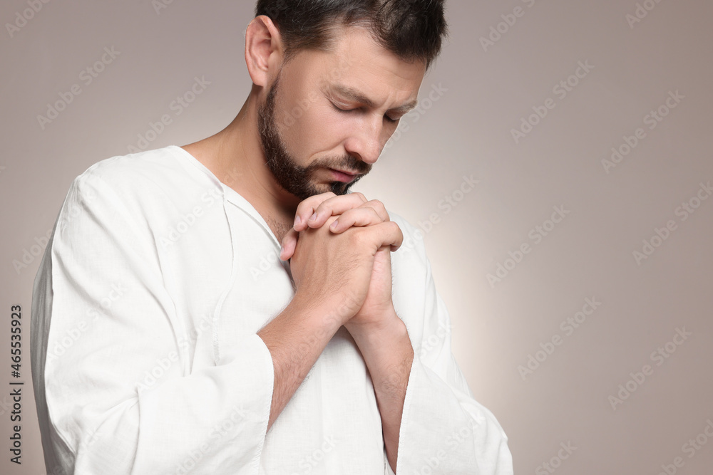 Religious man with clasped hands praying against grey background. Space for text