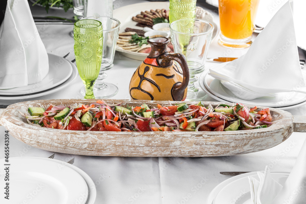 Fresh vegetable salad with tomatoes, red onion, cucumber and spices in wooden boat on the table
