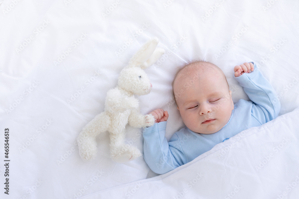 baby boy sleeping on the bed lying on his back with a stuffed toy hares in blue pajamas hands up, healthy newborn sleep baby boy sleeping on the bed lying on his back with a stuffed toy hares in blue pajamas hands up, healthy newborn sleep