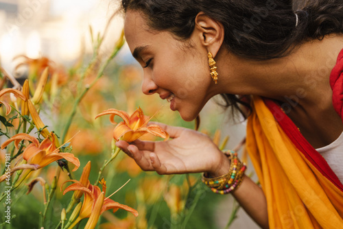 Schilderij op canvas Young indian woman wearing sari smiling while smelling flower