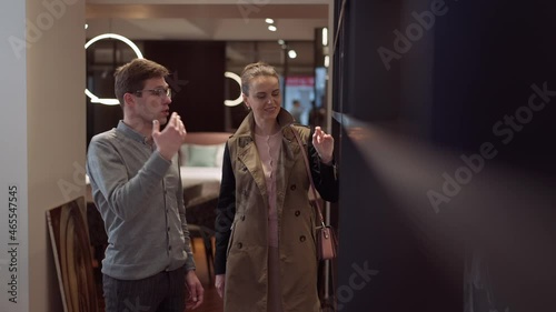 Smiling woman choosing cupboard listening man talking consulting client in furniture store. Positive rich confident Caucasian female buyer and male seller in shop. Consumerism concept photo